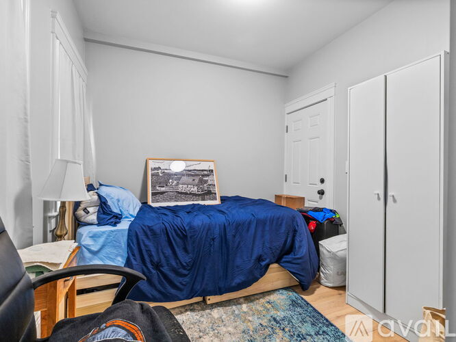 A bedroom with a bed covered in a blue blanket and a framed picture on the wall.