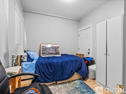 A bedroom with a bed covered in a blue blanket and a framed picture on the wall.