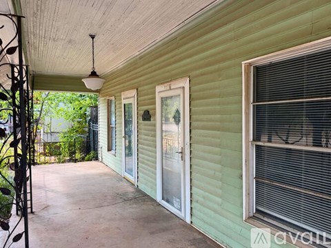 A porch with a swing hanging from the ceiling and a door with a window above it.
