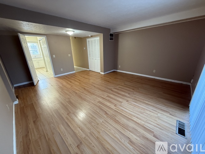 A spacious room with wooden flooring and two doors leading to other rooms.