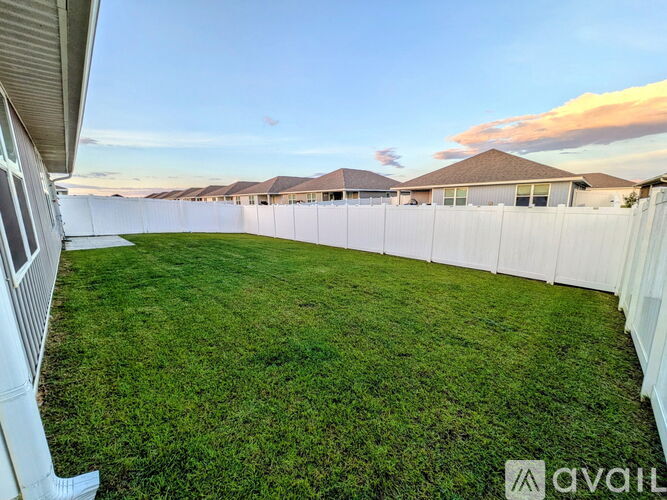 A backyard with a white fence and green grass.