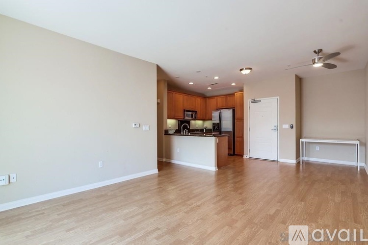 A spacious living room with hardwood floors and a kitchenette in the background.