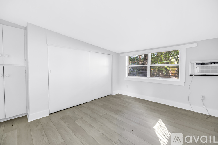 A room with white walls and a window showing a view of trees and a fence.