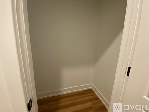 A white door with a black handle is open to a hallway with wooden floors.
