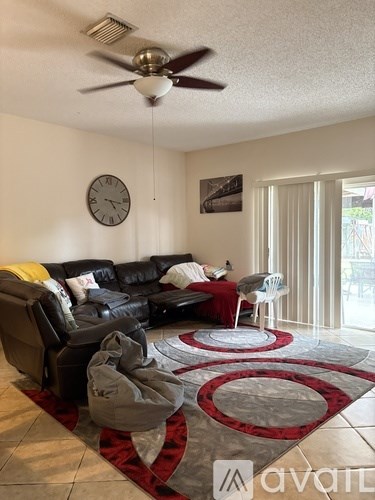 A living room with a black leather couch and a red and grey rug.