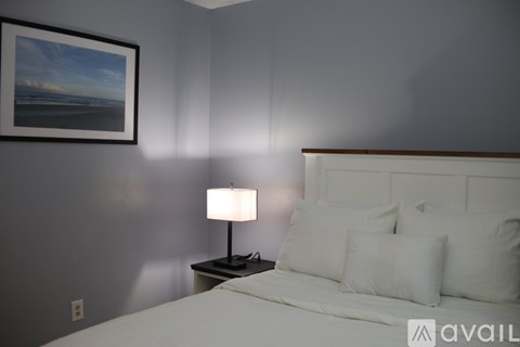 A bedroom with a bed, nightstand, lamp, and a picture on the wall.