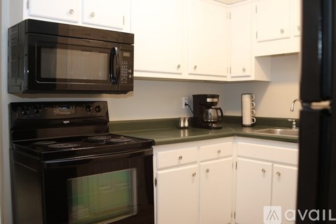 A black microwave oven is mounted above a black stove in a kitchen with white cabinets.