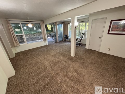 A living room with a carpeted floor and a view of a backyard through the windows.