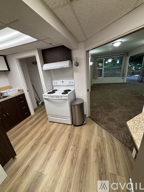A small kitchen with a white stove and a trash can.