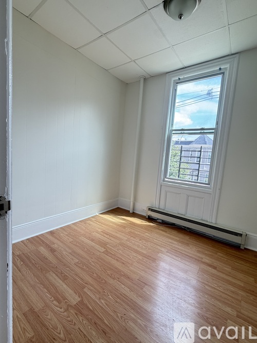 A room with wooden flooring and a window showing a fence and sky outside.