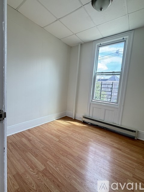 A room with wooden flooring and a window showing a fence and sky outside.