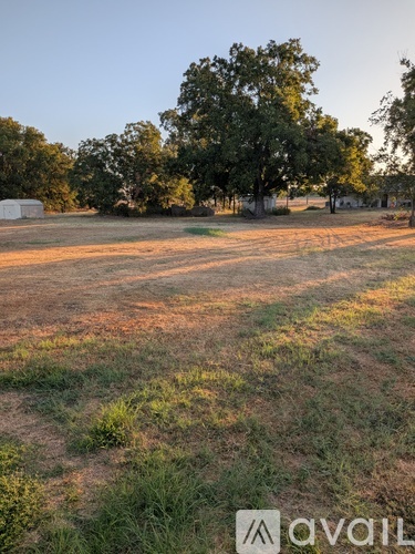 A field with trees and a white building in the background.