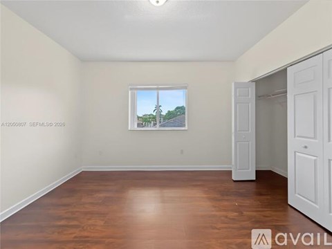 A room with wooden floors and a window showing a view of a street with cars and trees.