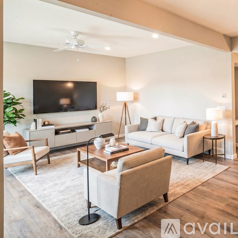 A living room with a white couch, a wooden coffee table, and a flat-screen TV mounted on the wall.