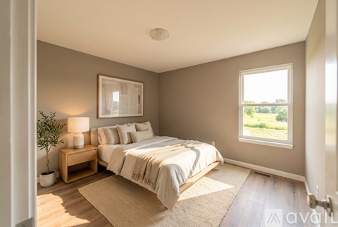 A well-lit bedroom with a large bed and a window showing greenery outside.