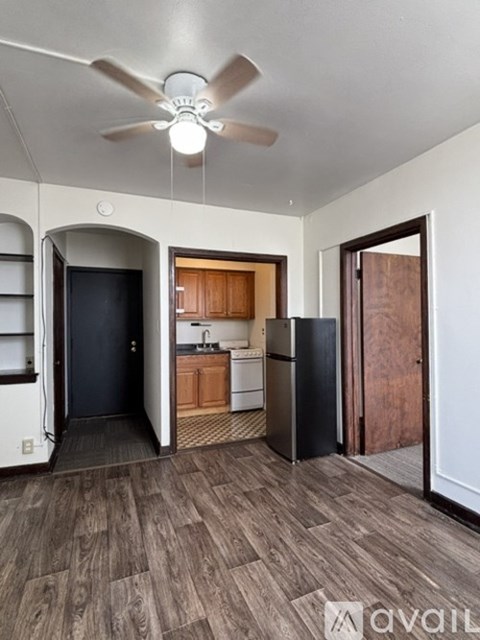 A room with a ceiling fan and a kitchen area with a sink and refrigerator.