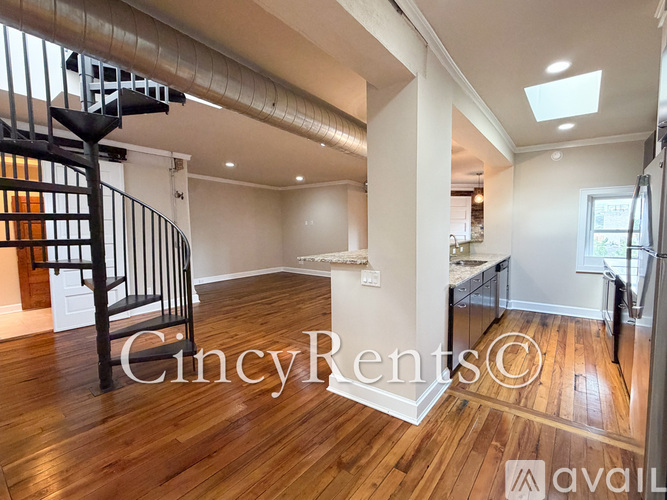 A spacious room with wooden floors and a staircase with a metal railing.