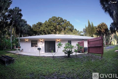 A house with a red door and a white exterior is surrounded by greenery.