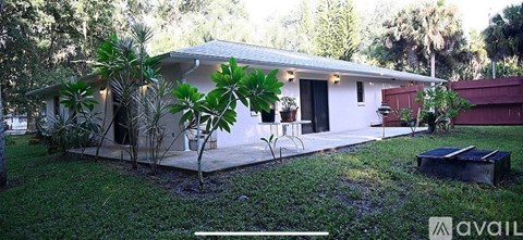 A house with a white exterior and a covered patio surrounded by greenery.