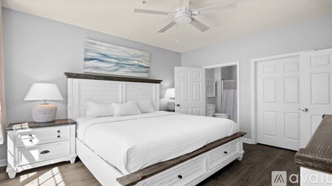 A bedroom with a large bed, a ceiling fan, and a nightstand with a lamp.