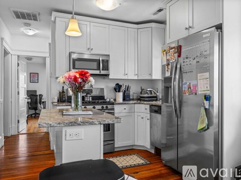 A kitchen with a refrigerator, microwave, and a table with a vase of flowers on it.