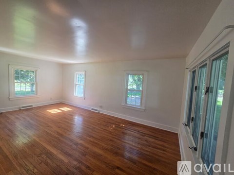 A room with wooden floors and white walls, with two windows and a door.