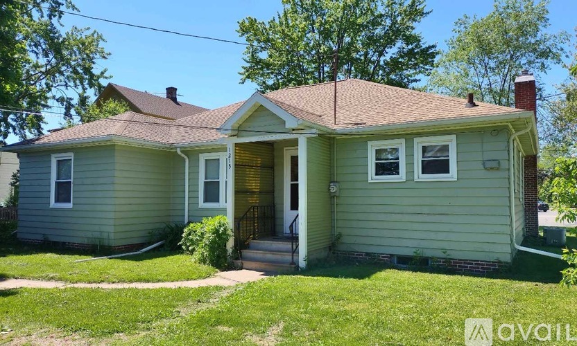A house with a green siding and a brown roof is for sale.