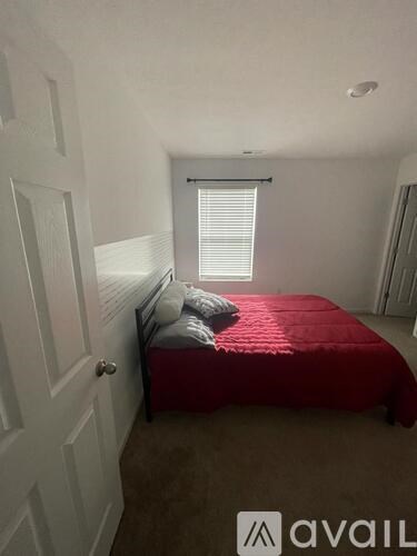 A bedroom with a red bedspread and a window with blinds.