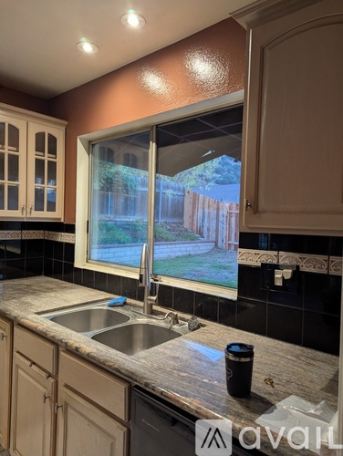 A kitchen with a sink and a window overlooking a backyard.