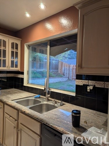 A kitchen with a sink and a window overlooking a backyard.