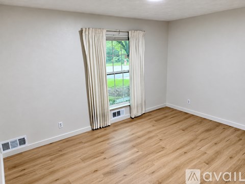 A room with wooden flooring and a window with curtains.