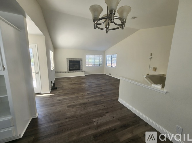 A large, empty room with wood flooring and a chandelier.