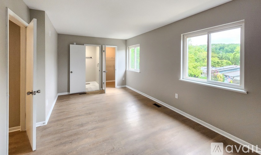 A spacious room with wooden floors and a large window overlooking a green landscape.