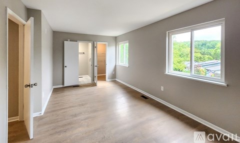 A spacious room with wooden floors and a large window overlooking a green landscape.