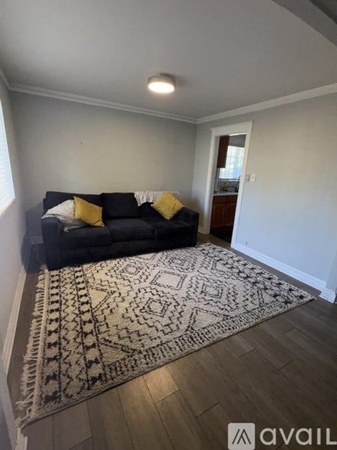 A living room with a black couch and a patterned rug.