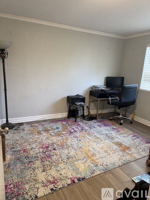 A room with a floral rug, a desk with a computer, and a chair.