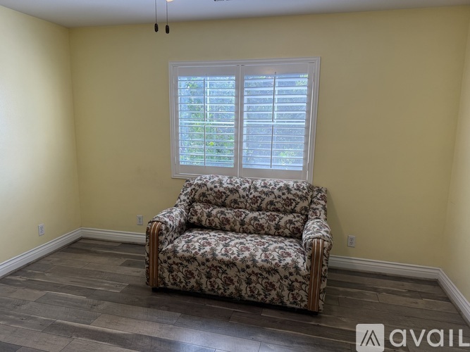 A floral patterned sofa sits in a room with a window behind it.