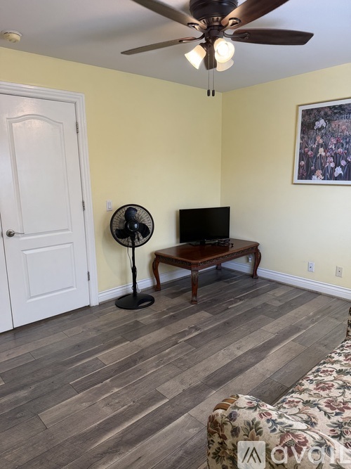 A room with a ceiling fan, a couch, and a television.