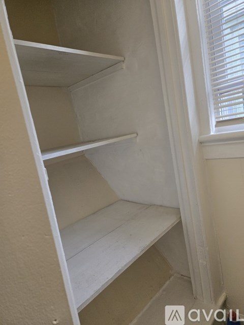 A white shelf unit with three shelves is in a corner with a window.