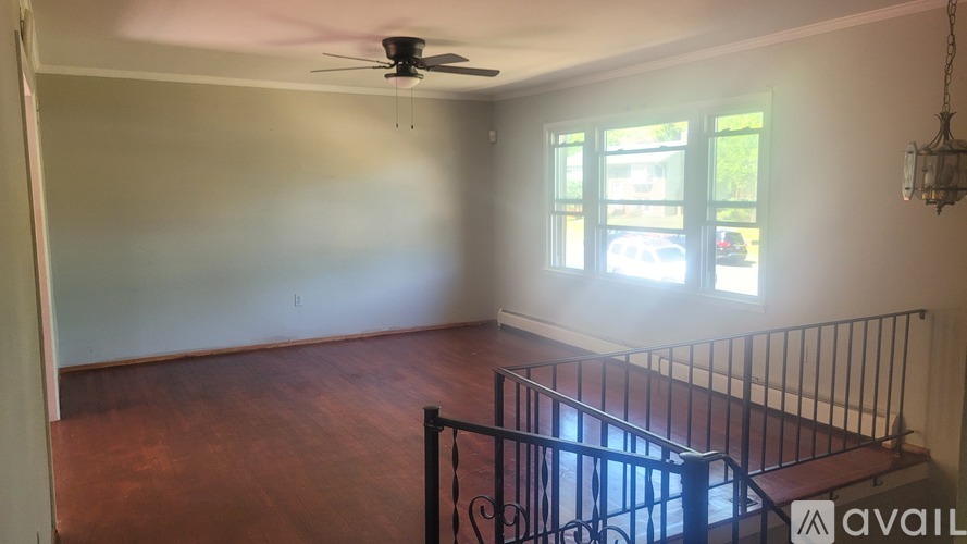 A room with a fan, wooden floor, and a staircase.
