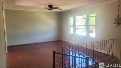 A room with a fan, wooden floor, and a staircase.