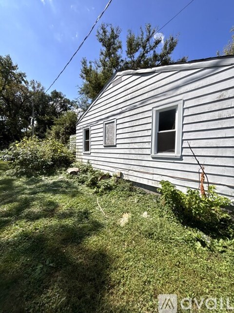 A house with a white siding and a window is surrounded by greenery.