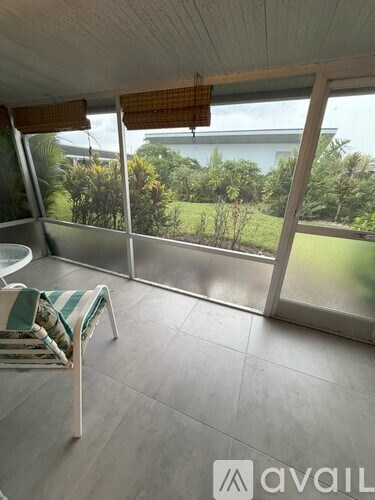 A room with a chair and a table in front of a window with a view of trees.