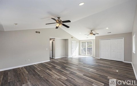 A spacious room with wood flooring and two ceiling fans.