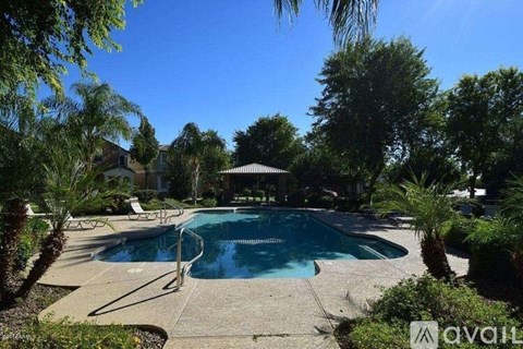 A pool surrounded by trees and plants with a house in the background.