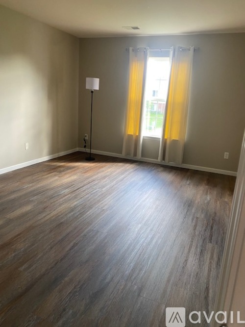 A room with wooden flooring and a window with yellow curtains.