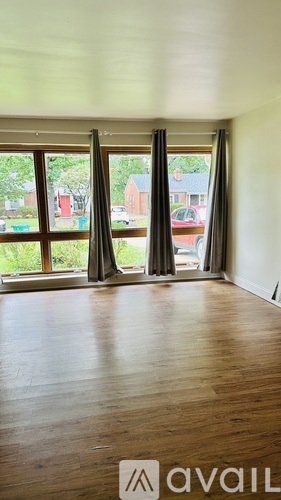 A room with wooden floors and a large window with curtains.