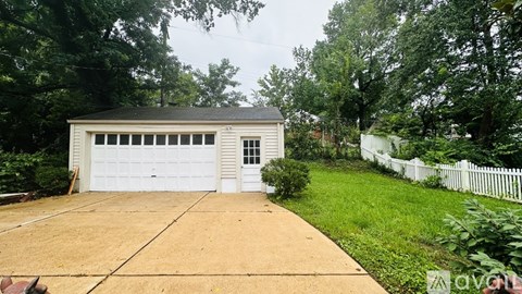 A detached garage with a white fence and a driveway in front.