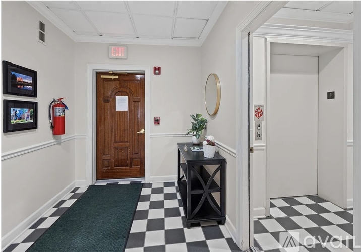 A hallway with a black and white checkered floor, a wooden door, and a red fire extinguisher.