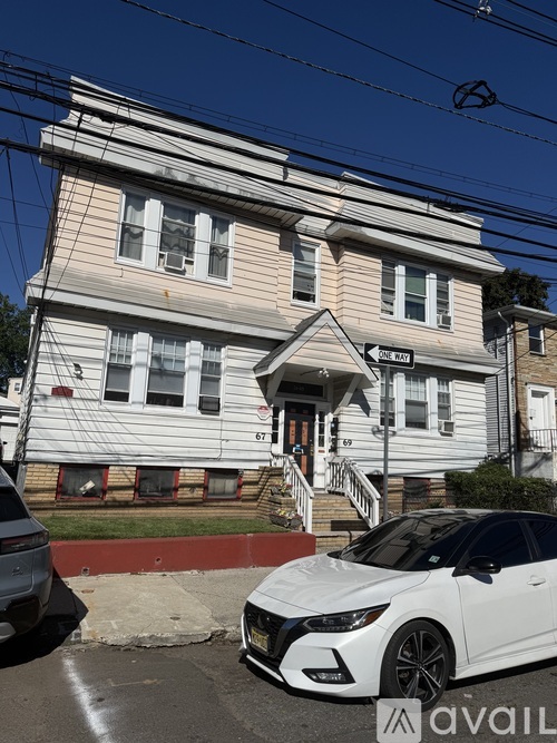 A white car is parked in front of a house with a sign that reads "AVAIL".